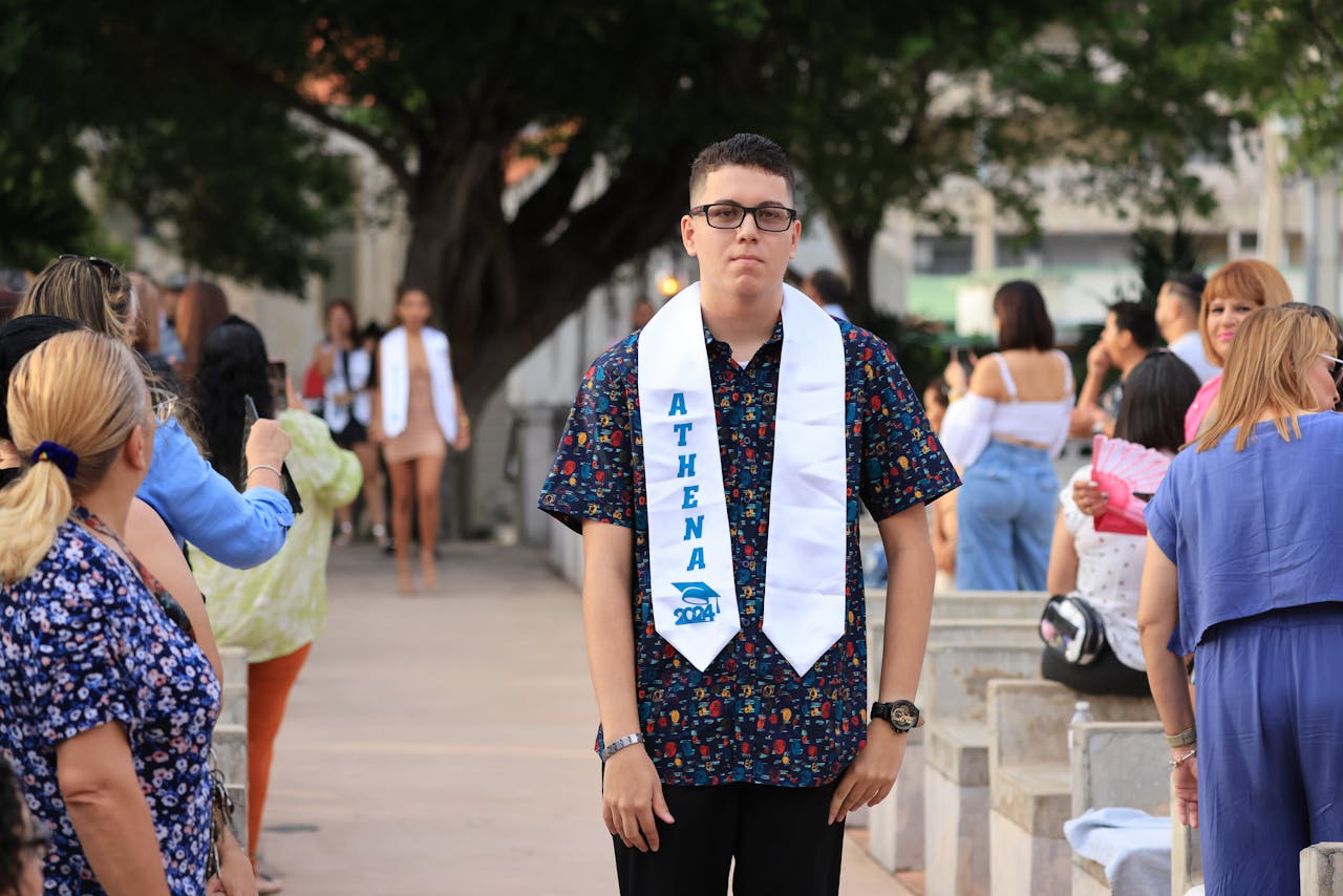 A young graduate stands with family and friends celebrating outdoors.